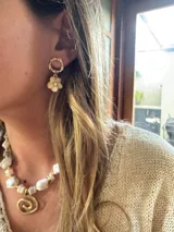 Aros colgantes dorados con dije de flor color crema.