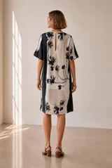 Vestido corto de corte recto y holgado, con mangas cortas y cuello redondo. Presenta un diseño estampado con bloques de color en tonos azul, blanco y negro, con detalles florales.