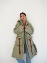 Abrigo largo acolchado color verde oliva, con capucha, cierre frontal con botones a presión y bolsillos con solapa y lazos decorativos.