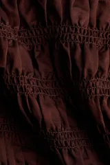 Top corto marrón con diseño fruncido en el cuerpo y las mangas largas, escote bote y terminaciones con volados sutiles en el cuello, los puños y el ruedo.