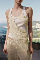 Top de cuello redondo y sin mangas, confeccionado en tejido de punto acanalado color crema. Presenta una aplicación asimétrica de tela tipo georgette en tono beige claro que cruza el frente de la prenda.