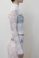 Remera negra de manga larga confeccionada en encaje, con cuello redondo y corte ajustado al cuerpo.