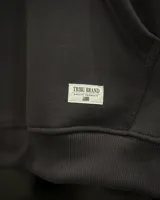 Canguro oversized color negro con estampado frontal en blanco que incluye dos soles y el texto "TRIBU BRAND".