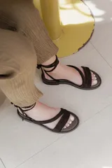 Sandalias bajas de cuero color marrón, con tiras finas para atar alrededor del tobillo.