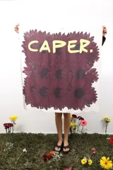 Pañuelo cuadrado de 1 metro por 1 metro, con estampado de flores bordó y texto "CAPER." en amarillo. Confeccionado en poliéster y elastano, es suave, flexible y tiene buena caída.
