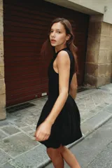 Vestido corto negro sin mangas, con cuello redondo y diseño de falda con volumen tipo globo. Presenta un corte entallado en el torso y cierre de cremallera oculta en la espalda.