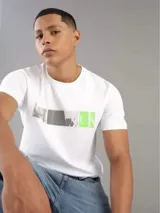 Remera blanca de algodón con cuello redondo y mangas cortas. Presenta un estampado gráfico frontal compuesto por bloques de color gris, negro y verde lima.