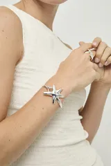 Pulsera rígida de metal bañado en plata con diseño de estrella de mar central y cierre de resorte.