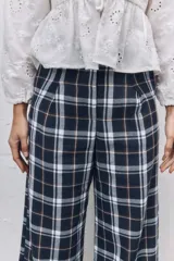 Pantalón sastrero de corte recto y tiro alto con estampado de cuadros escoceses en tonos azul marino, blanco y líneas finas en naranja. Presenta pinzas en la cintura y cierre frontal.