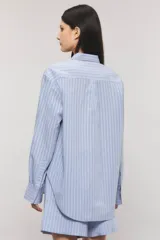 Camisa Sailor Line de calce holgado y diseño a rayas. Presenta cuello camisero, mangas largas y puños abotonados. Cuenta con acceso frontal mediante botones a tono y detalle bordado en el pecho.