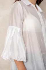 Camisa de organza blanca con cuello clásico, cierre frontal de botones y mangas tres cuartos abullonadas tipo globo con puños definidos.