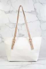 Bolso tipo tote bag de color blanco con textura granulada. Posee dos asas de hombro ajustables en color beige claro con hebillas metálicas.