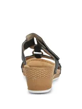 Sandalia Hush Puppies de plataforma baja con diseño de tiras negras. La tira delantera presenta un patrón geométrico calado con pequeñas tachas metálicas, mientras que la tira superior cuenta con un cierre de velcro para un ajuste personalizado. La plantilla es de color marrón y la suela tiene un acabado texturizado que simula madera.