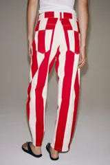 Jeans de tiro medio y corte tapered, con diseño de rayas verticales a contraste en color rojo y blanco. Cuenta con trabillas en la cintura, cinco bolsillos y cierre frontal con cremallera y botón metálico.