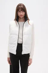 Chaleco acolchado blanco, sin mangas, con cuello alto y cierre frontal negro.