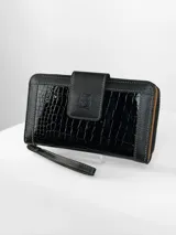 Billetera grande color negro con diseño combinado de cuero texturizado y cuero charolado con efecto reptil. Cuenta con cierre perimetral, solapa frontal con broche magnético y logo de búho grabado, e incluye una correa de mano extraíble.