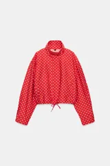 Chaqueta roja con estampado de lunares blancos, cuello subido, manga larga con puños plisados, bolsillos delanteros, bajo ajustable con cordón y cierre frontal con cremallera.