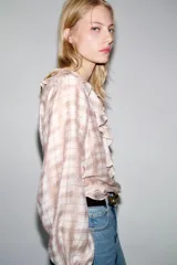 Blusa de manga larga abullonada con puños elásticos, cuello redondo con volantes y detalle de cordón ajustable en el escote pico. Presenta un estampado a cuadros en tonos blanco y rosado/marrón claro.