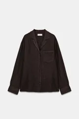Camisa de lino color negro, de manga larga, con cuello solapa y cierre frontal con botones. Presenta un bolsillo de parche en el delantero.