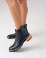 Bota corta de cuero vacuno color negro, con diseño de punta fina y cierre lateral. Presenta un taco bajo de madera y una entresuela de goma en tono natural que contrasta con el cuerpo de la bota.