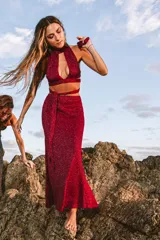 Pollera larga de tejido de punto color naranja con destellos brillantes, presenta un tajo frontal y una faja de ajuste en la cintura con lazo lateral.