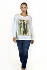 Remera blanca de manga larga con cuello redondo y estampado gráfico central que representa figuras estilizadas con detalles en tonos tierra y toques dorados.