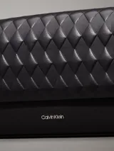 Cartera de hombro Calvin Klein negra con solapa acolchada con patrón de rombos. Posee correa de cadena metálica y logo metálico grabado en la parte frontal.