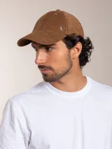 Gorro con visera color marrón de pana con logo de pájaro plateado en el lateral.
