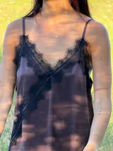 Vestido corto tipo lencero de seda color blanco, con detalles de encaje negro en el escote en V y en el ruedo asimétrico. Presenta breteles finos ajustables y una caída fluida.