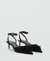 Zapato de tacón kitten color negro, con punta fina, tira ajustable al tobillo con hebilla y detalle de aplicación floral con flecos en el empeine.