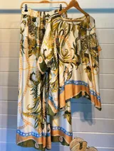 Blusa de satén con estampado de cadenas y hojas en tonos blanco, marrón y negro. Tiene corte amplio, mangas cortas y cuello redondo. Se ajusta a la cintura con un cinturón elástico negro con hebilla dorada.