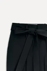 Pantalón negro de tiro alto con trabillas, bolsillos laterales y falsos bolsillos de vivo en la espalda. Incluye cinturón de lazo en el mismo tejido.