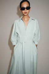 Vestido midi camisero de algodón color verde menta, con cuello camisero, manga abullonada por debajo del codo, cierre frontal con botones y lazo ajustable en la cintura.