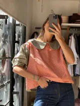 Blusa bicolor de pana elastizada con mangas cortas abullonadas, cuello redondo amplio y diseño estampado con combinación de tela roja con motivos florales pequeños y mangas y cuello en tono gris con estampa similar.