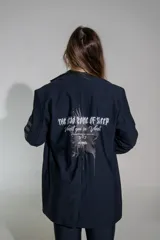 Blazer de lycra color negro, con diseño de solapas amplias y bordados de alas en el frente. Presenta un corte holgado y moderno con mangas largas.