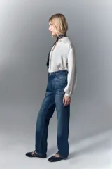 Jean de corte recto y tiro alto confeccionado en denim azul rígido. Presenta un diseño de hotfix brillante aplicado sobre la superficie del pantalón. Cuenta con cierre y botón frontal.
