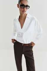 Pantalón chino de tiro bajo color marrón oscuro, con pernera recta y bajo con vuelta. Incluye un cinturón trenzado delgado de color marrón claro. Cuenta con bolsillos delanteros y cierre frontal con cremallera y botón.