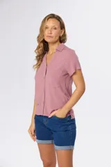 Camisa lisa de lino color beige, de manga corta, con cuello camisero, bolsillo ojal en el pecho y cierre frontal con botones.