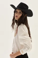 Camisa blanca de algodón con bordados florales en tonos rosados y rojizos en el frente. Presenta mangas largas abullonadas y puños con bordado.