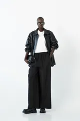 Chaqueta semi-larga negra con acabado brillante o efecto charol, cuello camisero y frunce ajustable en la cintura. Presenta cierre frontal y bolsillos prácticos.