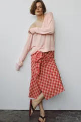 Falda midi de tiro medio ZARA WOMAN COLLECTION confeccionada en hilatura con algodón, con estampado de cuadros en tonos rojos y blancos. Presenta detalle de pliegue con lazadas en el delantero y bajo recto con abertura. Cierre con cremallera oculta en costura.