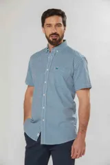 Camisa de manga corta a cuadros vichy en tonos verde y blanco, con cuello abotonado y bolsillo frontal.