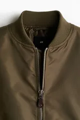 Campera bomber de nylon levemente acolchada, con cuello, puños y bajo acanalados. Presenta cierre frontal, bolsillos laterales con botón a presión y un bolsillo con cierre en la manga.