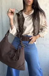 Chaleco de gamuza color chocolate con bordados decorativos en hilo claro y detalles de tachas metálicas en el frente. Presenta cierre frontal con botones forrados.