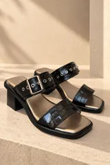 Sandalias de cuero vacuno negro con textura efecto cocodrilo, punta cuadrada y taco bloque. Presentan una tira ancha con hebilla metálica plateada y ojalillos decorativos.