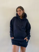 Hoodie oversize color negro con capucha y cordones ajustables. Presenta un bolsillo frontal tipo canguro y detalles de etiquetas en las mangas. El diseño incluye un estampado gráfico de un león en la espalda.