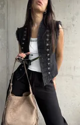 Chaleco negro de denim estilo militar, con doble botonadura metálica frontal, cuello alto y detalles deshilachados en las sisas.
