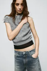 Jersey de punto gris jaspeado con cuello redondo y manga corta. Presenta detalles de encaje en los laterales.