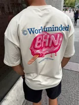 Remera de corte oversize color beige, con estampado gráfico en la espalda que presenta un helado de palito rosa con la inscripción 'BHN' y el texto 'Worldminded' en azul.