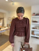 Blusa color chocolate con diseño de frunces elásticos en el frente y la espalda, mangas largas abullonadas con puños elásticos y corte peplum.